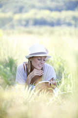 Naklejka na ściany i meble Smiling woman laying in grass and reading book