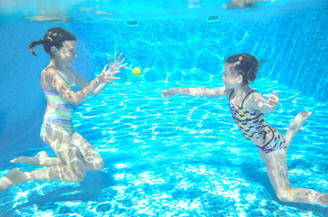 Happy kids swim in pool and play underwater having fun