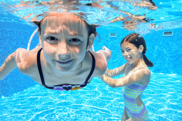 Happy kids swim in pool and play underwater having fun