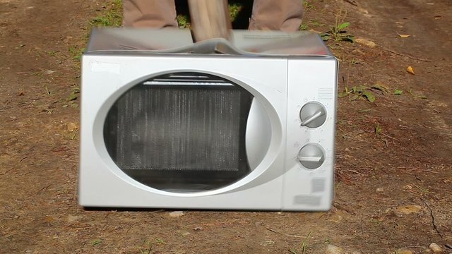 Man with sledge hammer destroying microwave oven