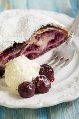 Plate with cherry strudel and fork on blue table.