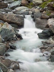 Naklejka na ściany i meble Noisy Alpine stream with with stones. Blurred waves of stream 