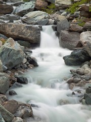 Noisy Alpine stream with with stones. Blurred waves of stream 