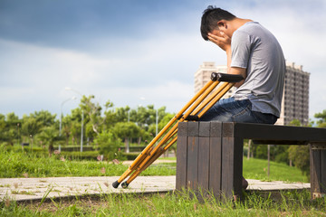 Injured Man with crutches sitting on a bench