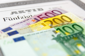 Aktie mit aufgefächerten Geldscheinen und Tiefenschärfe
