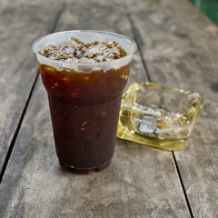 Delicious ice coffee americano  with cigarette on the old wooden