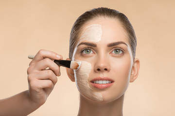 Beautiful girl in spa applying facial cosmetic cream with brush