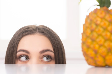 Happy young housewife looking at fresh pineapple.