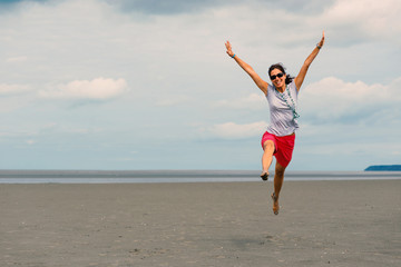 Happy woman jumping on the beach in front of Mont Saint Michel a