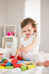 Cute girl playing with building blocks on bed