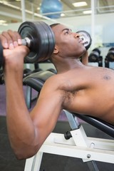 Fototapeta na wymiar Shirtless young man exercising with dumbbells in gym