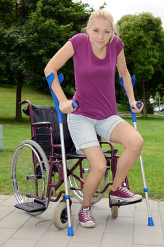 Frau erhebt sich an Krücken aus Rollstuhl