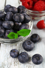 Glass bowls of raspberries and blueberries on wooden background