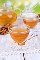 Teapot and cups of tea on table on bright background