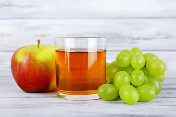 glass of juice with fresh grape and apple on grey wooden table