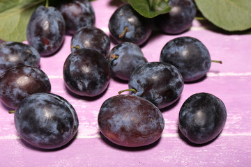 Ripe sweet plums with leaves, on pink wooden table