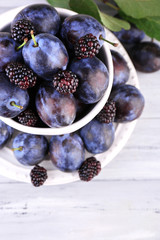 Ripe sweet plums in big cup, on grey wooden table