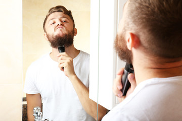 Obraz premium Young man shaving his beard in bathroom