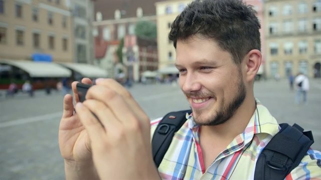 Young man with beard taking picture with cellphone in a city.