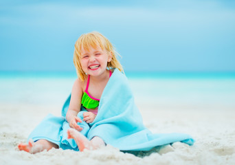 Portrait of smiling baby girl in towel sitting on beach