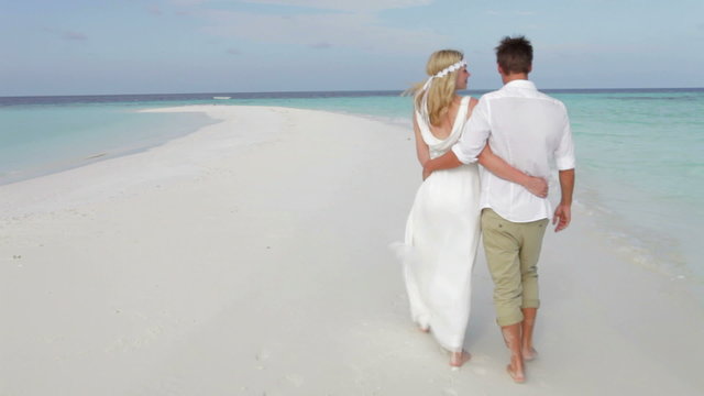 Rear View Of Couple Walking Along Beach At Wedding