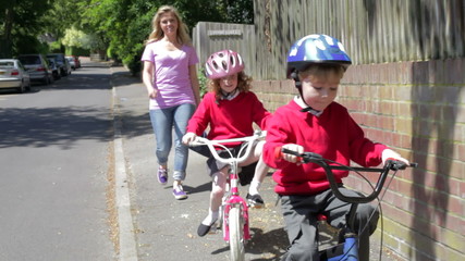Children Riding Bikes On Their Way To School With Mother