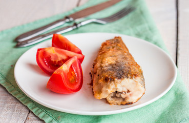 Shad grilled fish with tomato on a plate, fork and knife