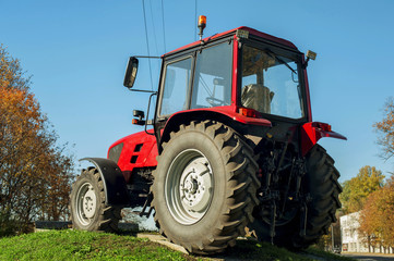 Modern red tractor on a blue sky background. Outdoors.