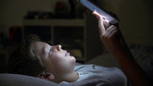 Boy Looking At Digital Tablet In Bed At Night
