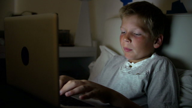 Boy Using Laptop Computer In Bed At Night