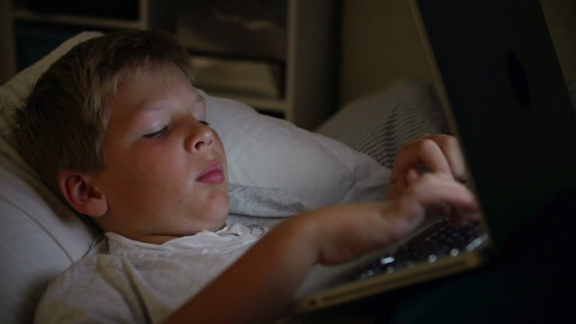 Boy Using Laptop Computer In Bed At Night