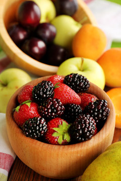 Ripe fruits and berries in bowl on table close up