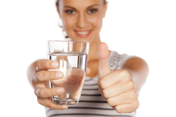 a young woman holding a glass with water and showing thumb up