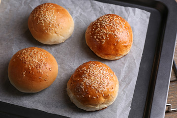 Tasty buns with sesame on oven-tray, on wooden background