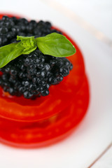 Slices of tomato with black caviar on plate closeup