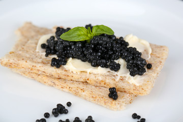 Slices of bread with butter and black caviar on plate closeup