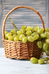 Ripe grapes in wicker basket on wooden table on light