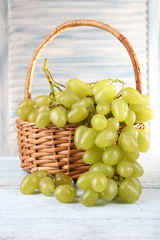 Ripe grapes in wicker basket on wooden table on light