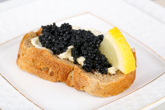 Slice of bread with butter, black caviar and lemon