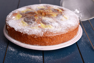 Delicious cake and sieve with powdered sugar on wooden table