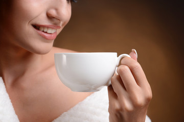 Beautiful young girl with cup of coffee on brown background