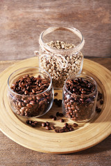 Coffee beans in jars on bamboo plate on wooden background
