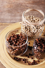 Coffee beans in jars on bamboo plate on wooden background