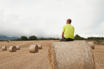 Naklejka na ściany i meble Young man in a field with straw bales. Resting on a bale