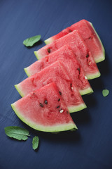 Watermelon slices with mint leaves over dark blue wooden surface