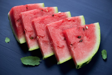 Sliced watermelon with fresh mint, dark blue wooden background