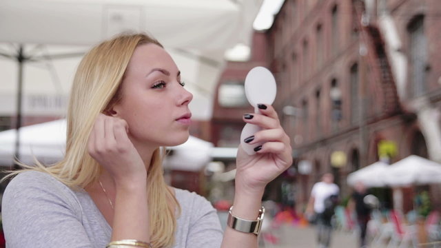 Young attractive woman applying make up outdoors