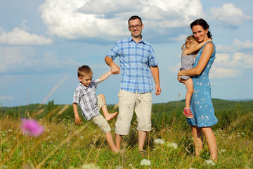 happy young family of four having fun on the top of a hill 
