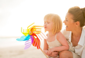 Mother and baby girl playing with colorful windmill toy on the b © Alliance
