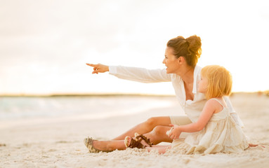 Baby and mother pointing on copy space while sitting on beach